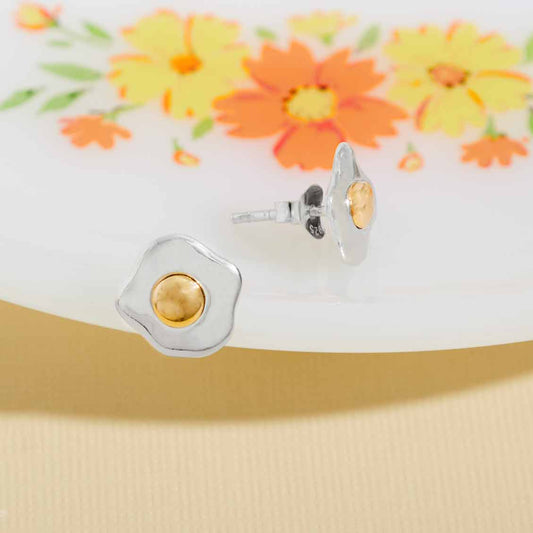 Silver and gold stud egg earrings on a floral background