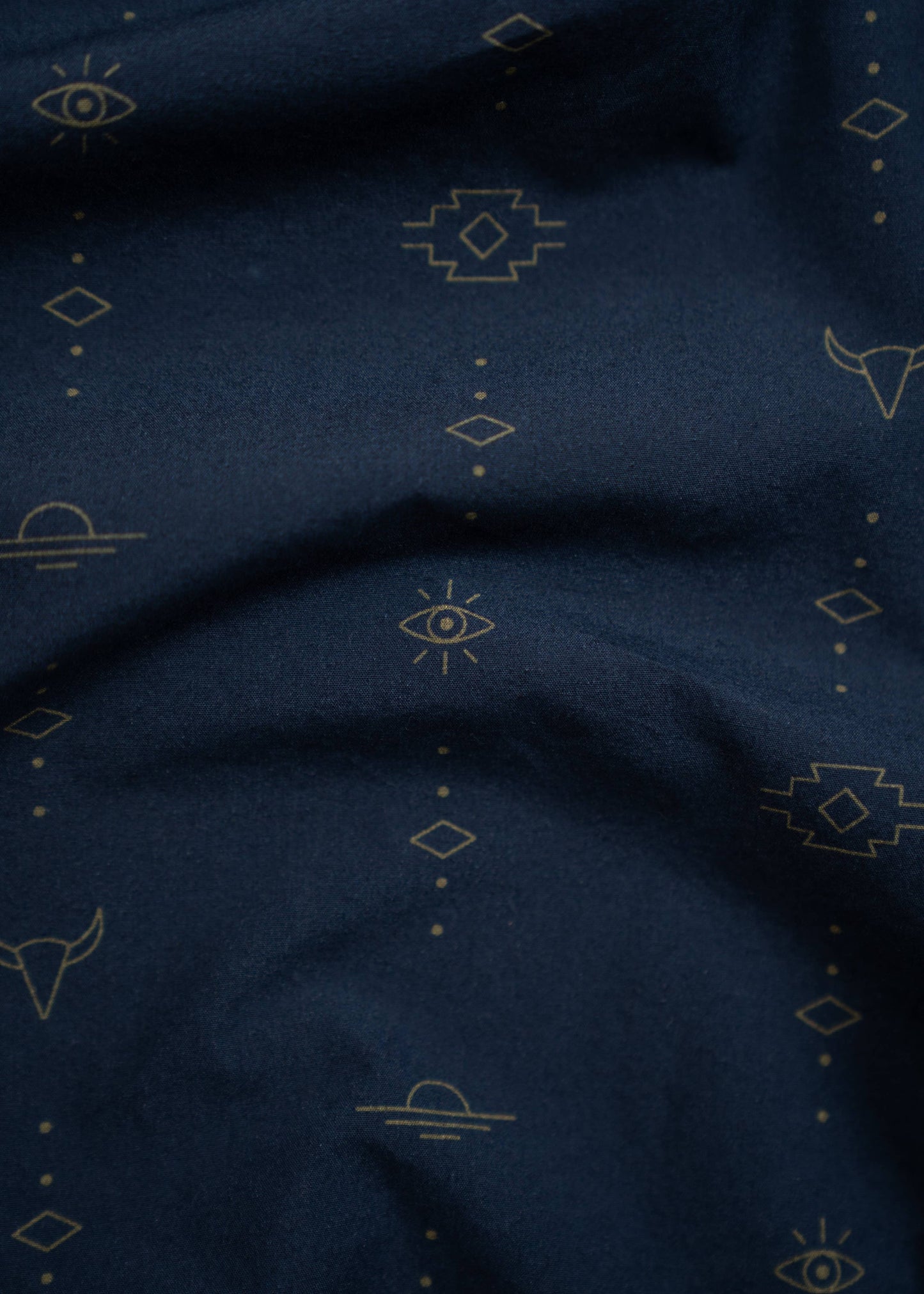 close up of small patterns on navy western shirt including eyes, longhorns, sun and dot designs