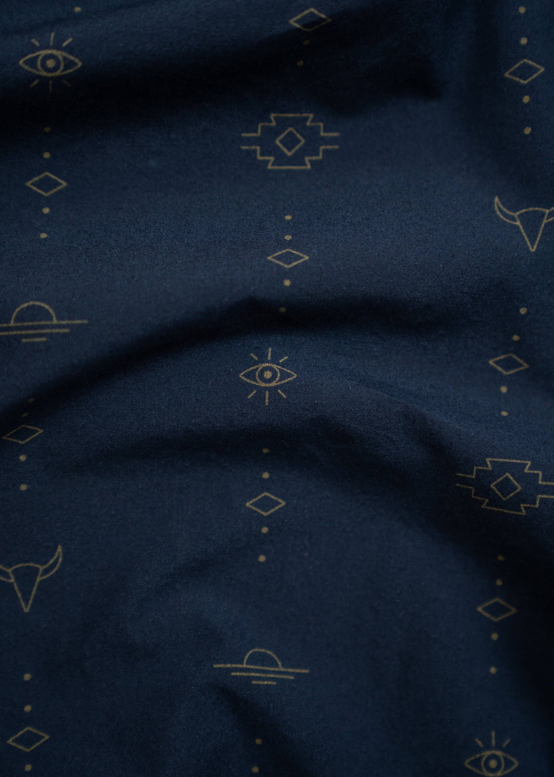 close up of small patterns on navy western shirt including eyes, longhorns, sun and dot designs
