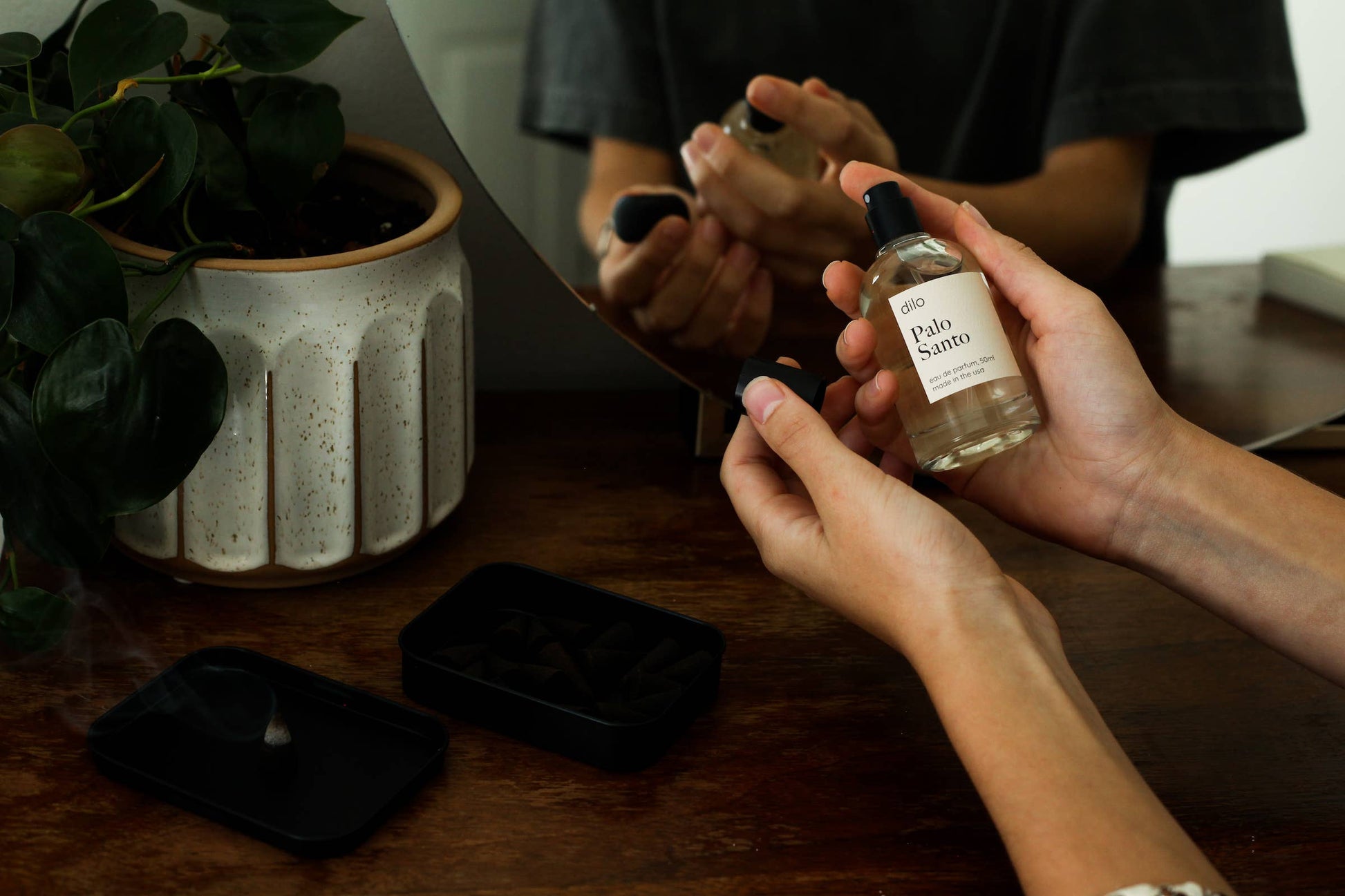 Two people holding small bottles with a plant and a box in the background