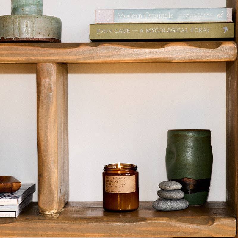 Wooden shelf with books, a candle, and a green vase against a white wall.