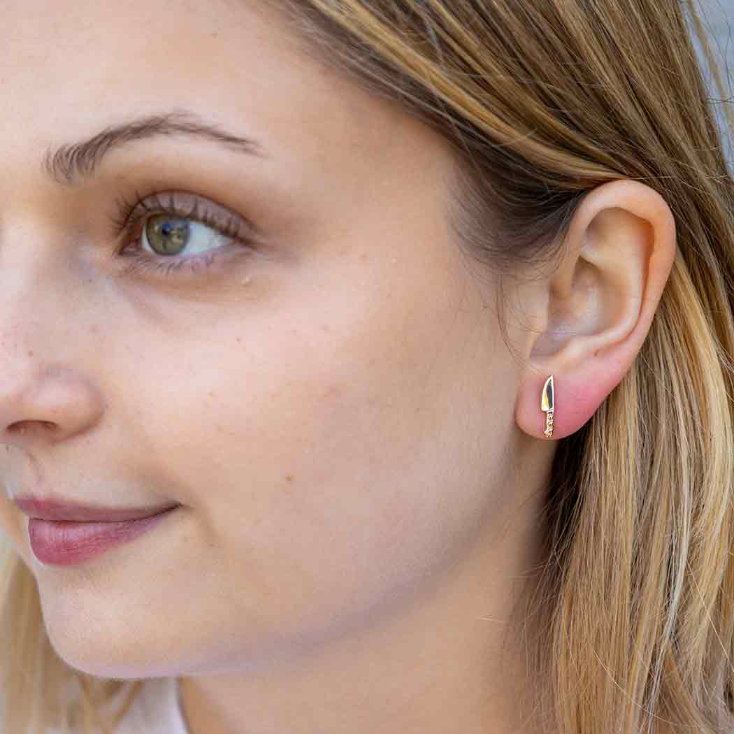 close up of model wearing a small gold knife shaped earring