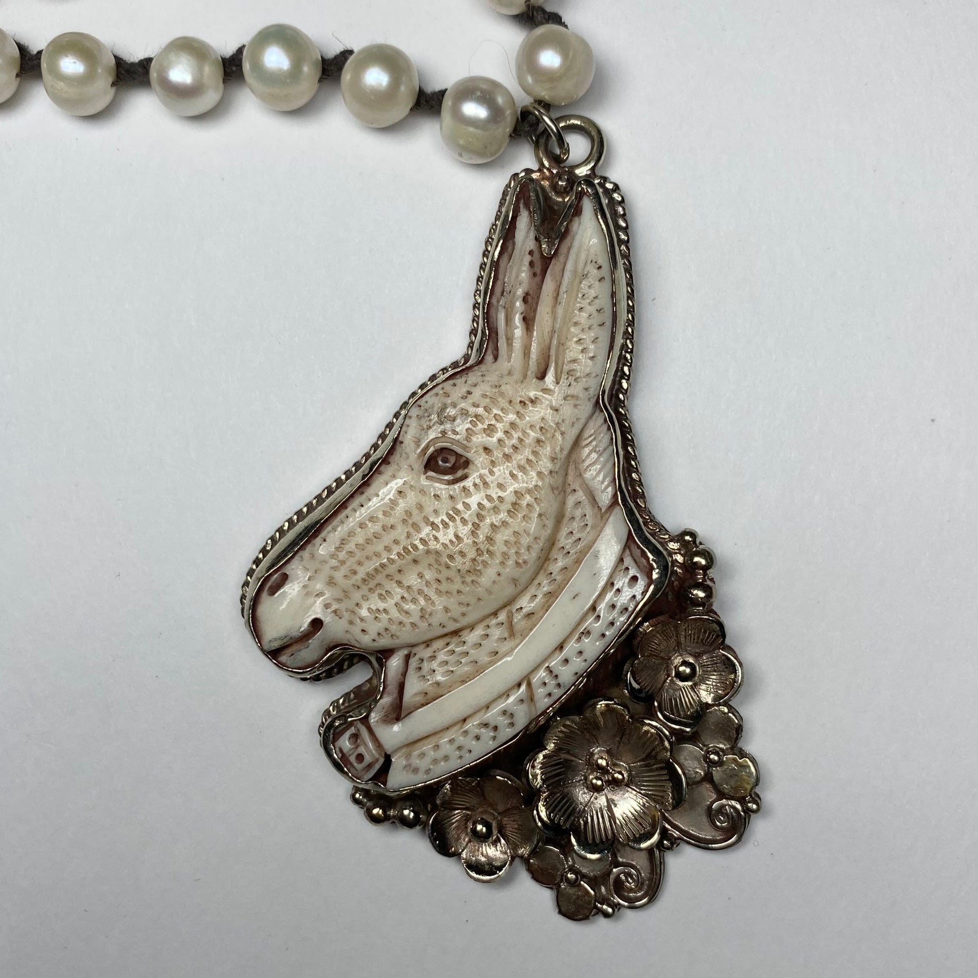 Close up of a carved donkey with silver flower pendant.