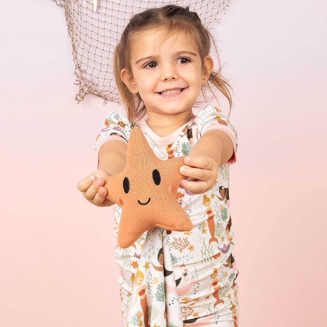Child holding a star-shaped plush toy against a pink background
