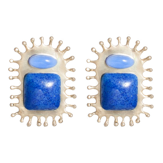 A pair of silver stud earrings featuring a textured, crown-like silver border with small spikes, a smaller oval light blue stone at the top, and a larger square deep blue stone at the bottom, set against a plain white background.