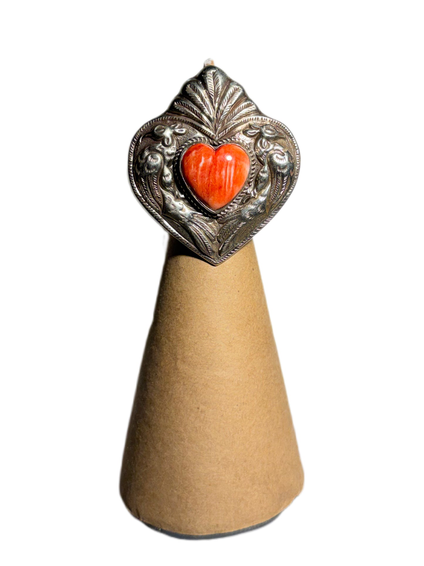 Decorative ring with a heart-shaped red stone and silver top on a beige stand against a white background