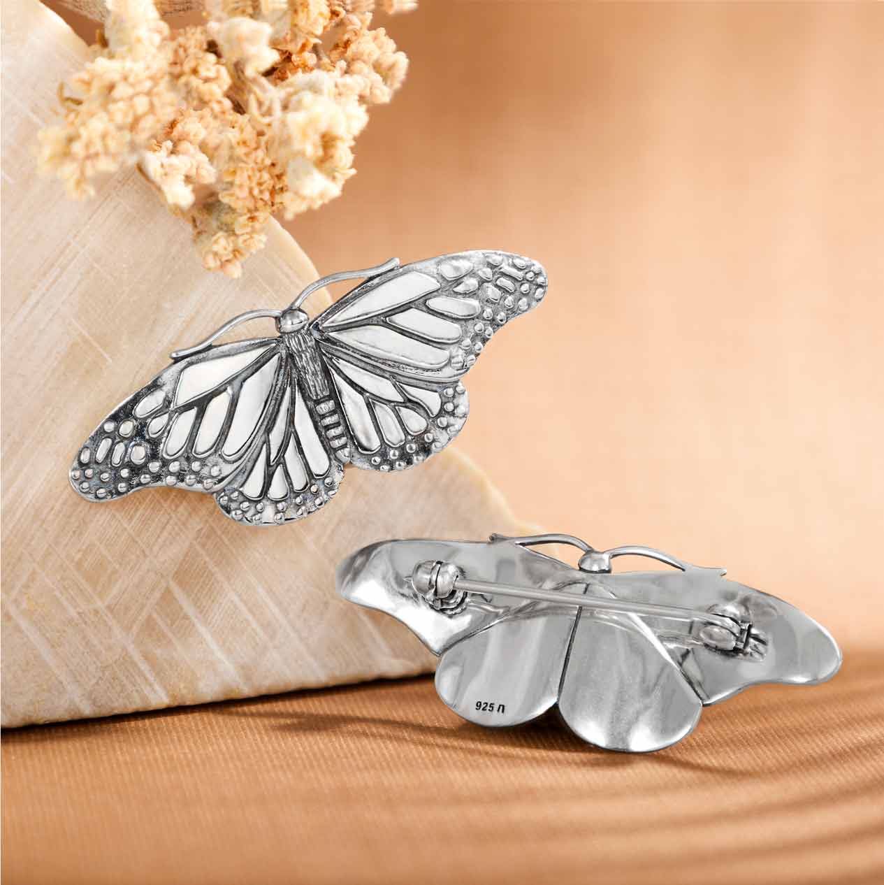 A sterling silver brooch designed in the shape of a monarch butterfly with gently curved wings, displayed against a beige background.