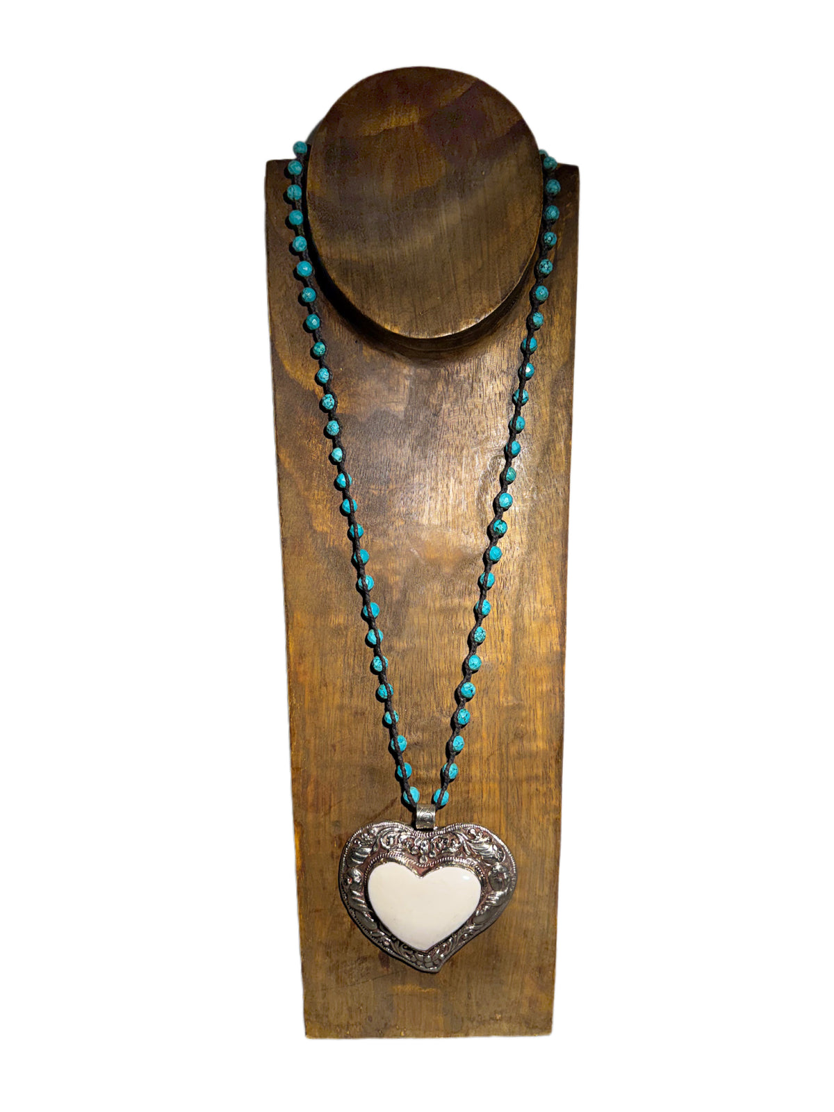 A heart-shaped bone pendant necklace with a silver border hanging from a turquoise beaded chain on a wooden display stand against a white background.