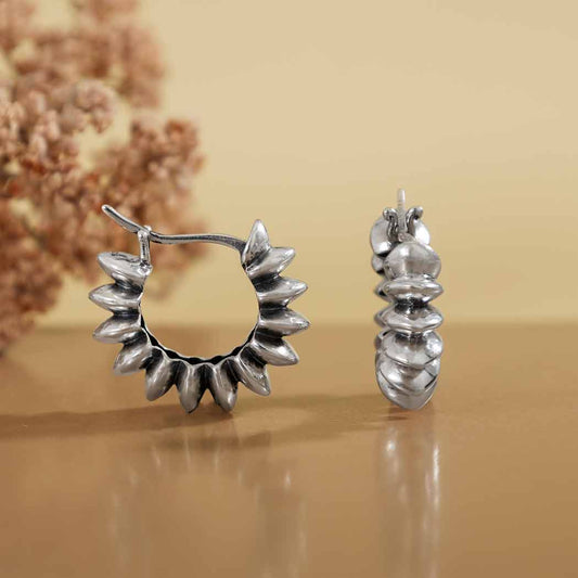 Pair of silver hoop earrings on a beige surface with a blurred floral background