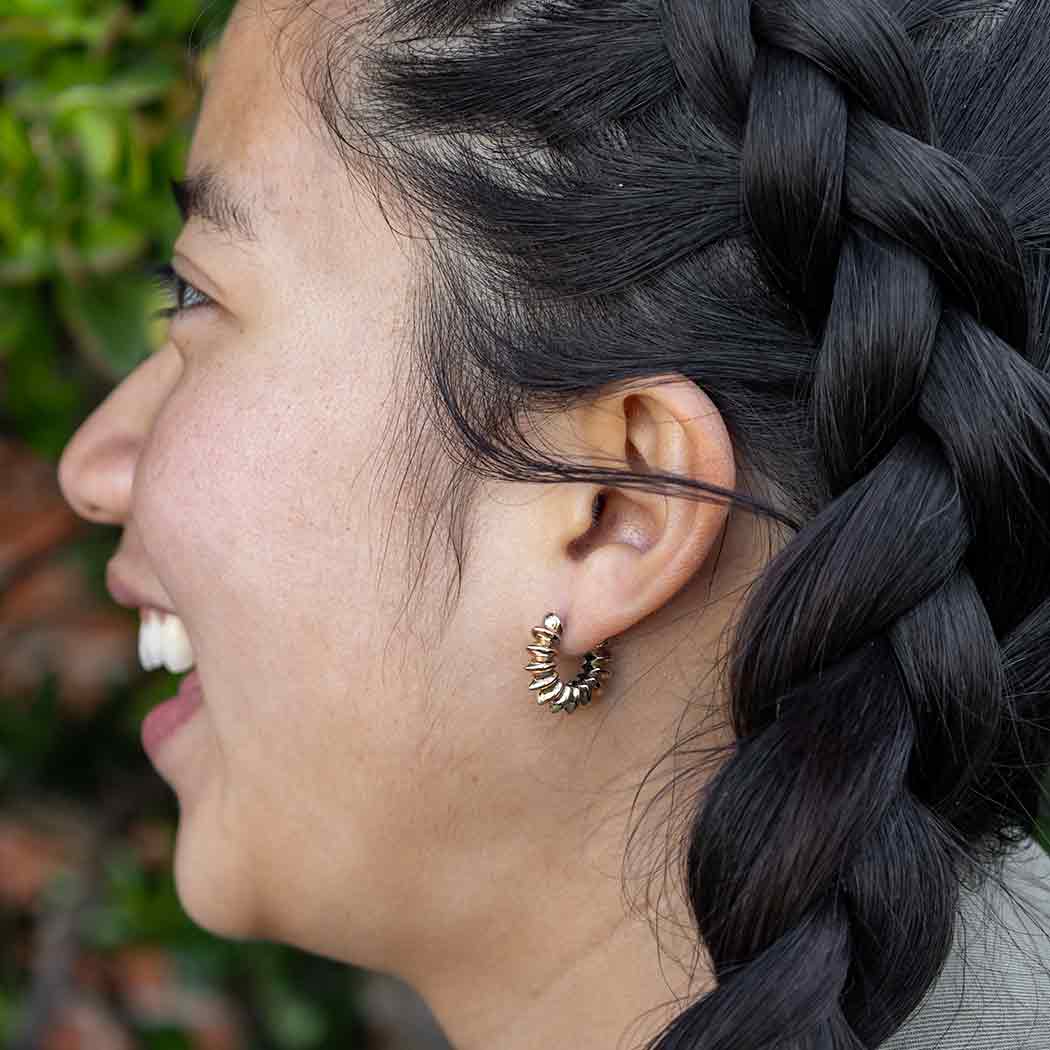 Close-up of a person with braided hair wearing a gold earring, with a blurred natural background.