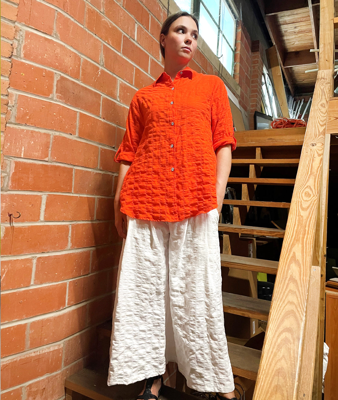 model in a wide leg white textured pant with a matching coral color button down blouse with rolled sleeves held with a small tab. black and white buttons.