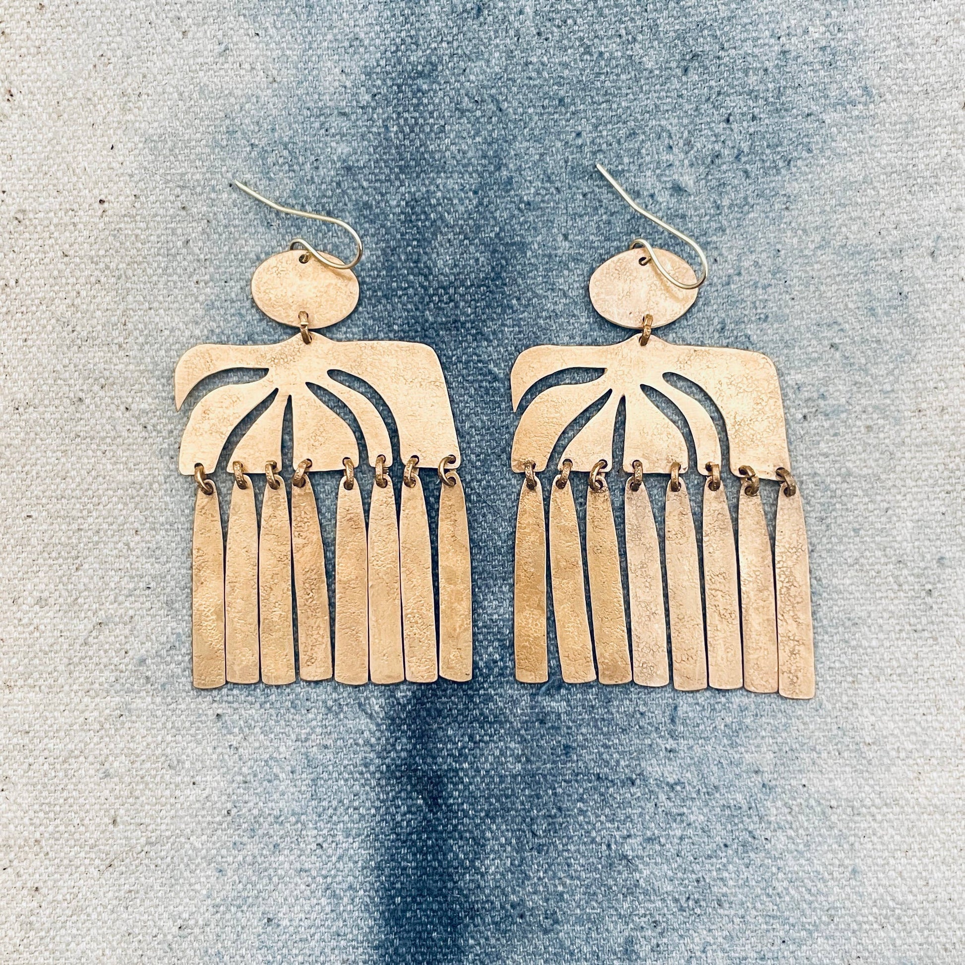 Pair of gold fringe earrings on a textured blue surface