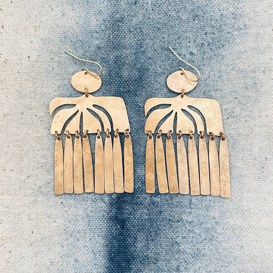 Pair of gold fringe earrings on a textured blue surface