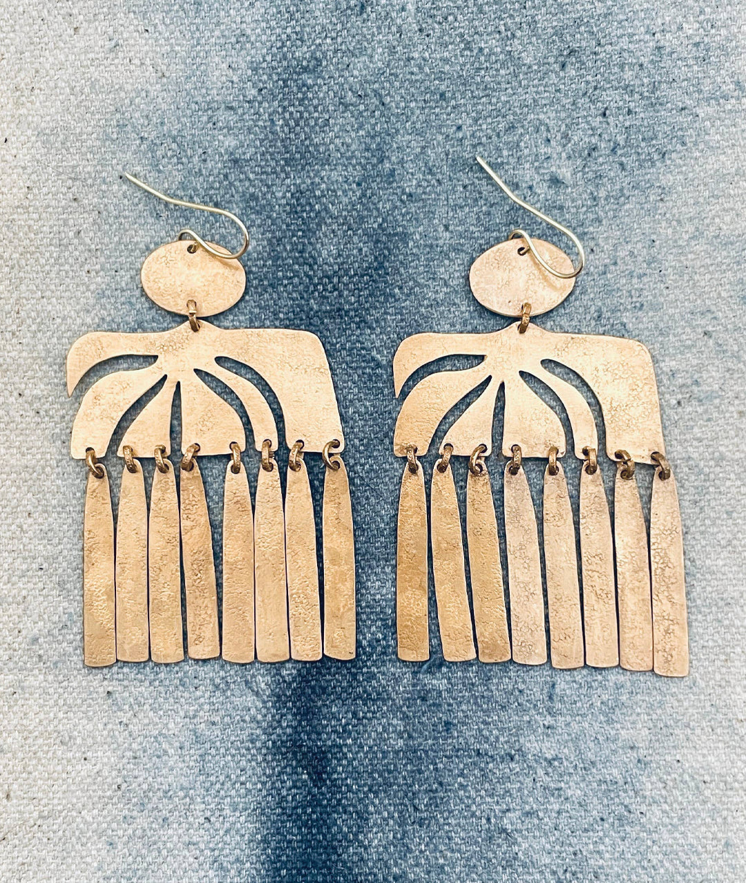 Pair of gold fringe earrings on a textured blue surface