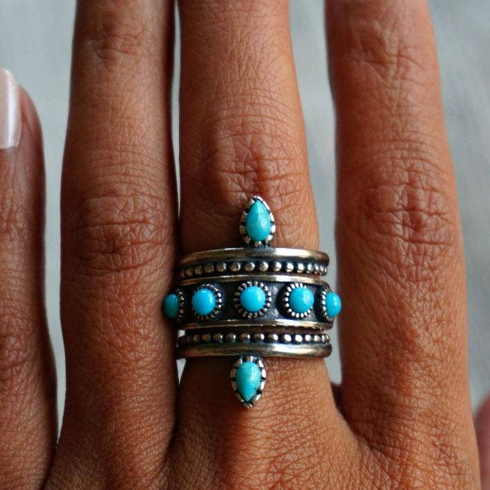 Turquoise and silver ring on a person's finger with a neutral background