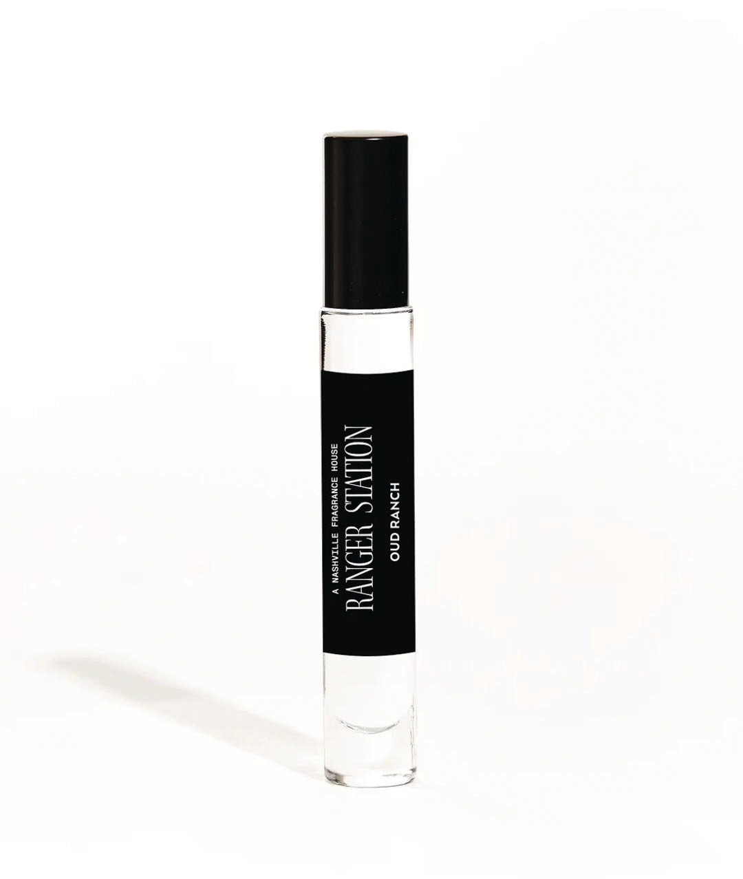 A small, cylindrical bottle of Oud Ranch Quickdraw Perfume with a black label and white cap, labeled with the brand's name and the scent 'Palo Santo / Oud Wood / Cedar / Pepper'.