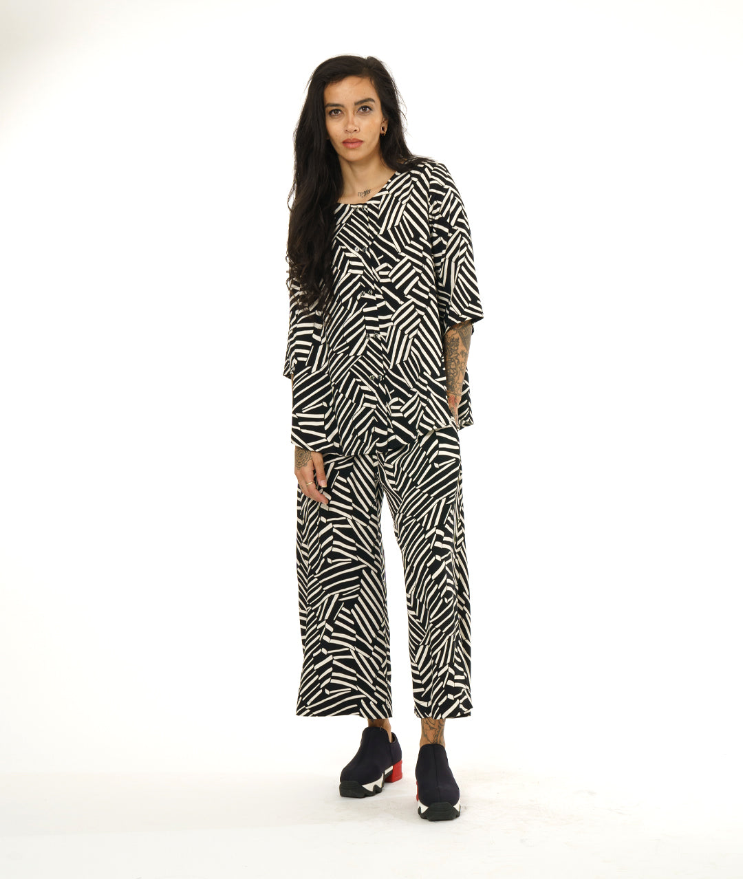 model in a black and white broken stripe print pant, worn with a collar less matching fabric button down blouse with 3/4 sleeves