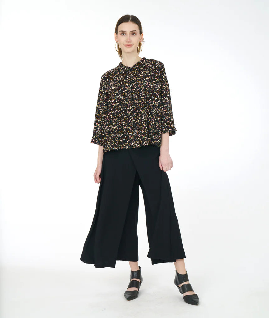 model wearing black terrazzo print top with double sets of "twin" buttons down the front, easy a-line shape and straight hem. sleeves are 3/4 sleeve with open cuff. inverted pleat and open notched collar in back. paired with black pants and shoes.