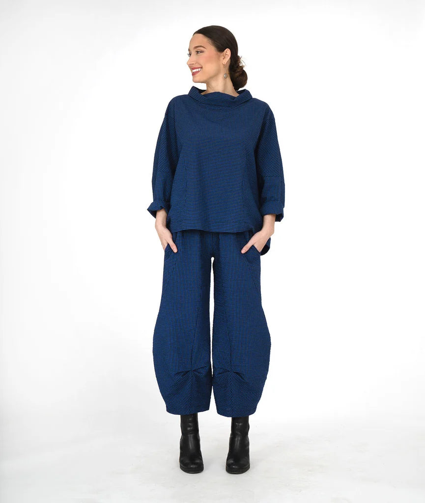 A woman modeling a matching navy blue two-piece outfit consisting of a loose long-sleeve top and wide-leg tapered pants, paired with black ankle boots, against a plain white studio background.