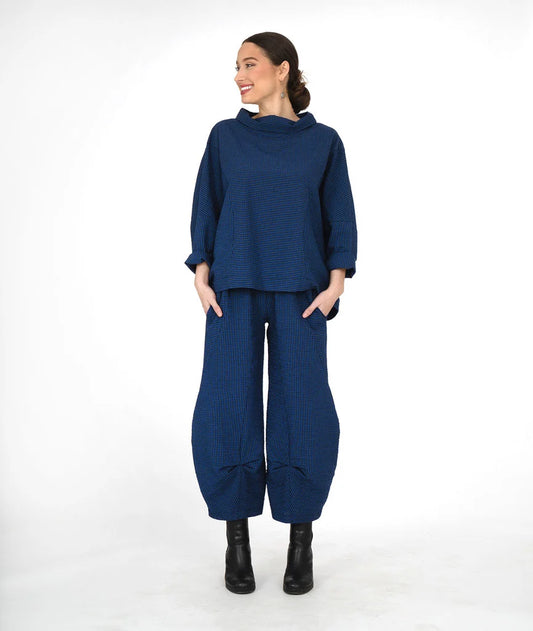 A woman modeling a matching navy blue two-piece outfit consisting of a loose long-sleeve top and wide-leg tapered pants, paired with black ankle boots, against a plain white studio background.