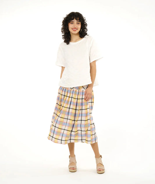 model wearing full gathered skirt with elastic waist and bias cut yoke in a plaid pastel pattern paired with white tshirt and sandals