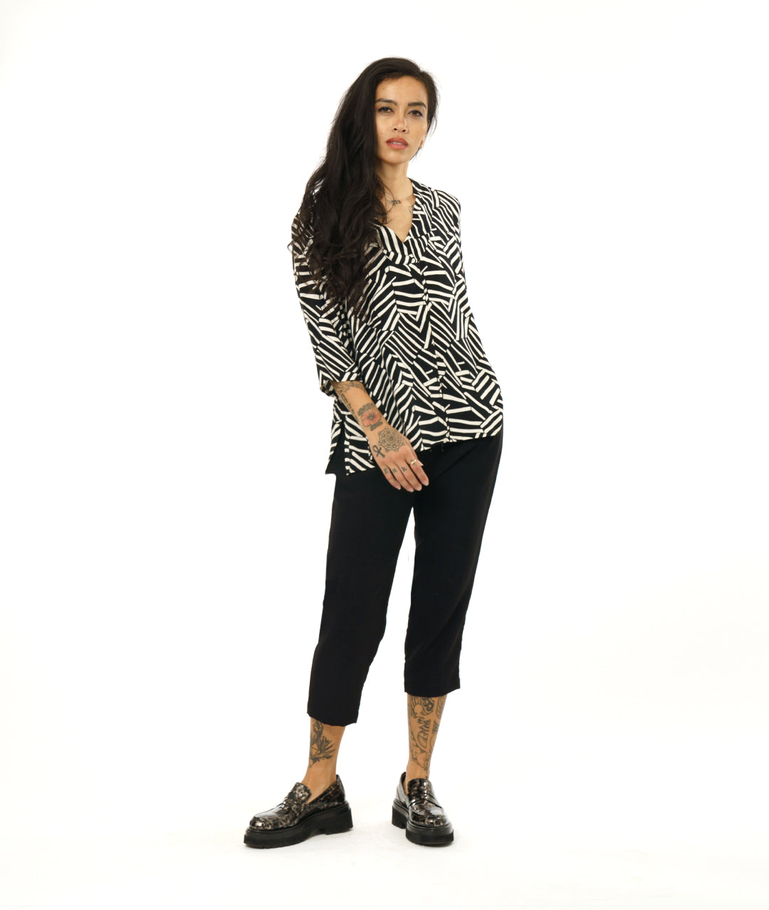 model in a black and white broken stripe print pullover top with 3/4 sleeves and a v-neck. worn with a simple black crop pant