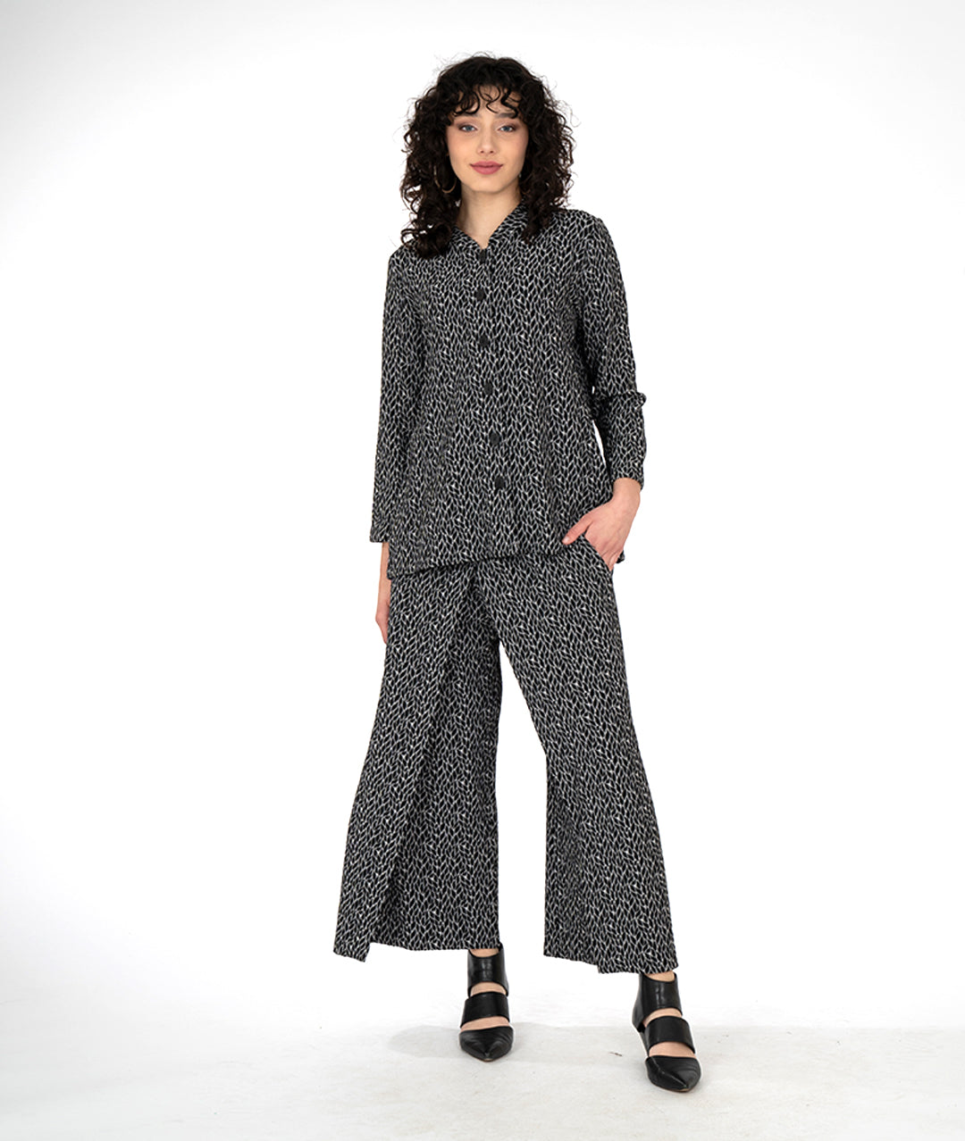 model in a wide leg grey and black leaf print pant with an overlapping front, worn with matching button down blouse with a standing collar and long sleeves