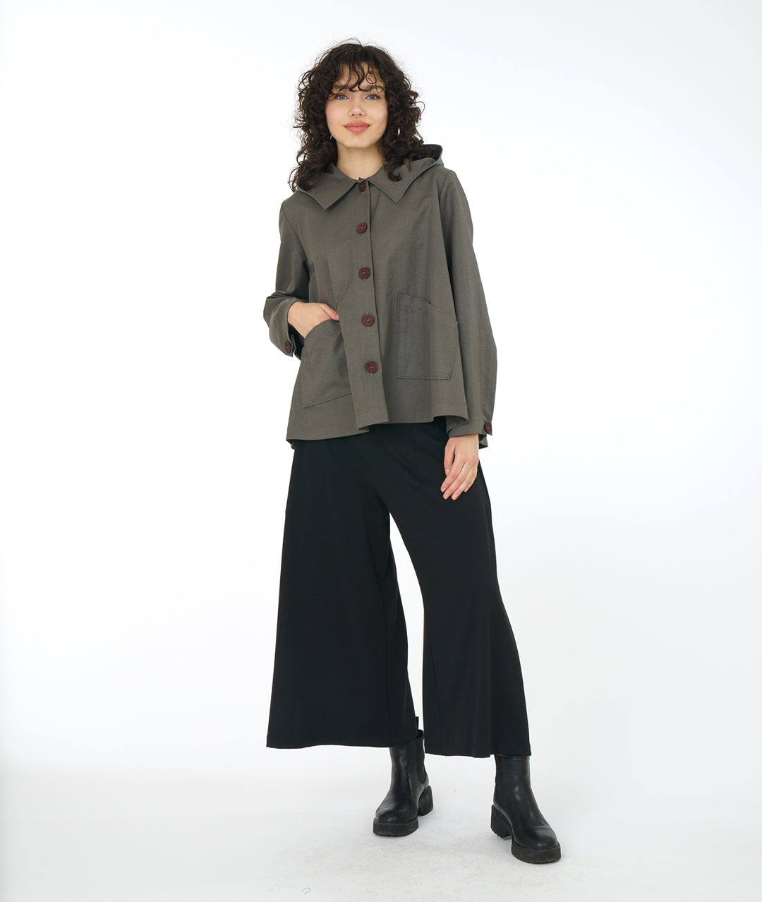 model in a grey/green boxy hooded jacket, worn with a wide leg black ankle length pant