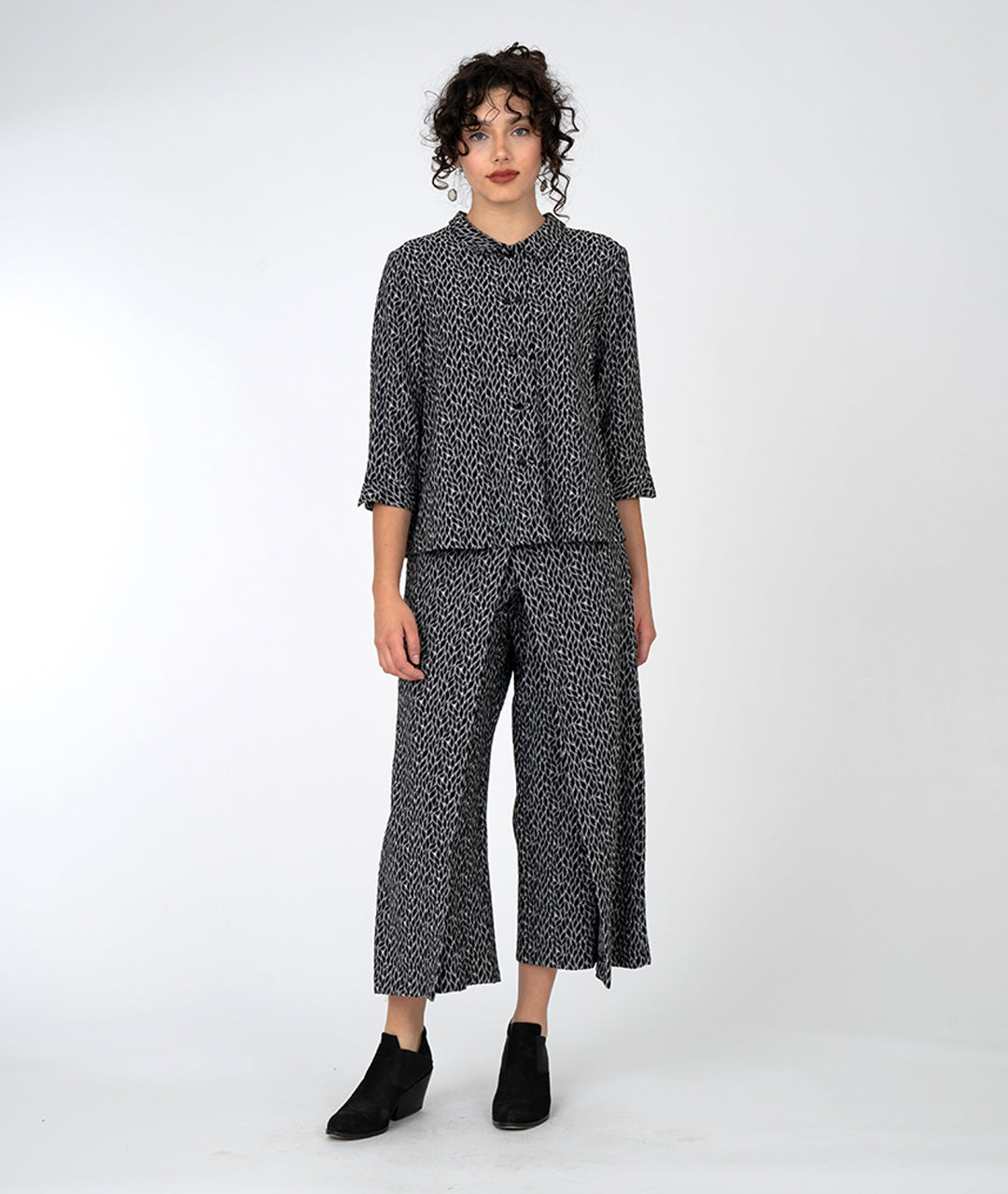 model in a wide leg black and grey leaf print pant with an overlapping front, worn with a matching button down with a twin button and 3/4 sleeves