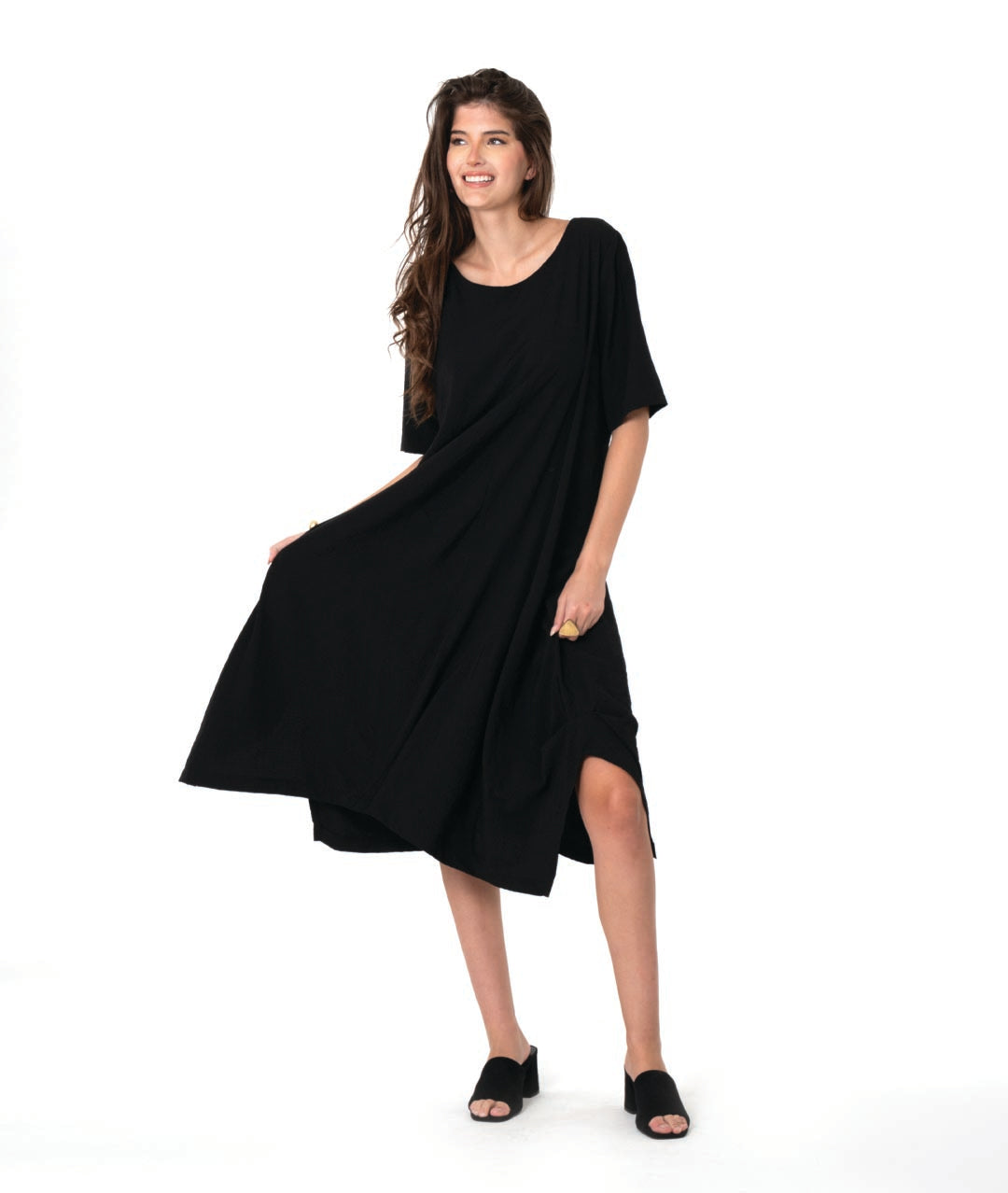 model in a pullover black dress with a slight grid texture. dress has a rounded neck, elbow length sleeves, and a flowy skirt with tucks and splits