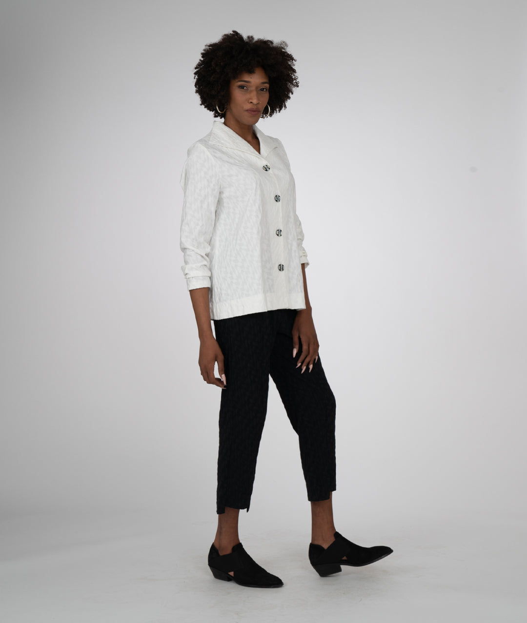 model in a white blouse and a straight leg black diamond knit pant with a stair-step hem