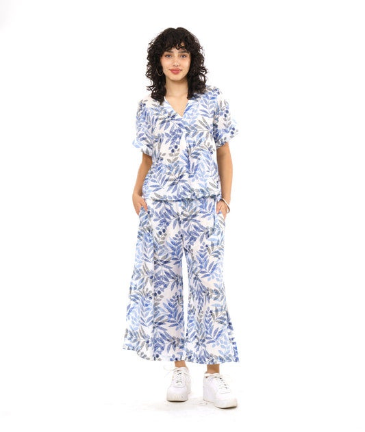 model in a white boxy pullover with a blue and black leaf print. worn with a matching wide leg pant with a slit up either side