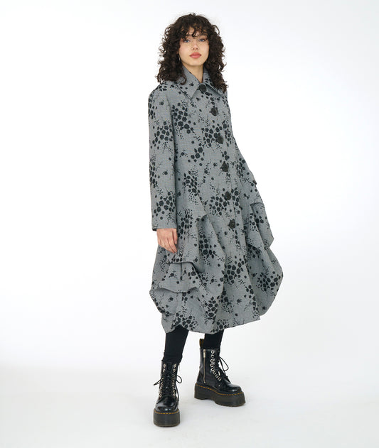 model in a grey plaid coat with a black pollen print. coat has oversized buttons and collar, and a full body at the hips from large tucks at the side and princess seams