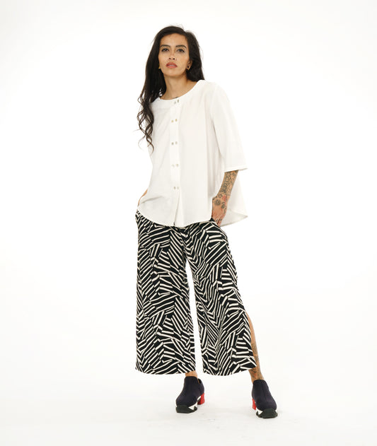 model in a black and white broken stripe print pant with a long slit at the side seams, worn with a collar less white button down blouse with 3/4 sleeves