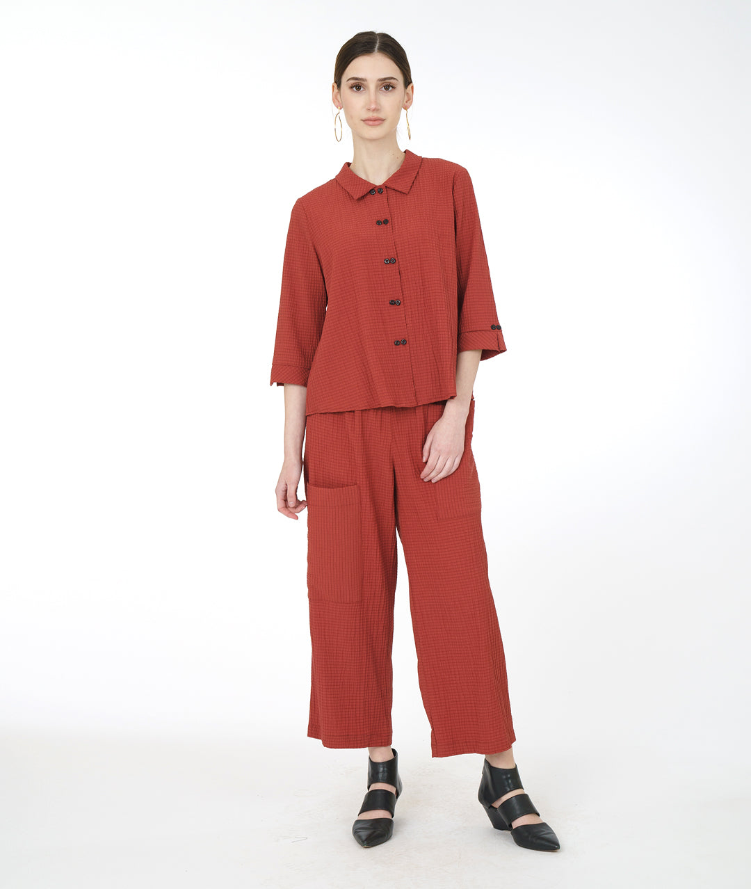 model in a sienna color pant with asymmetrical cargo pockets, worn with a matching button down top with 3/4 sleeves and a twin button detail up the front