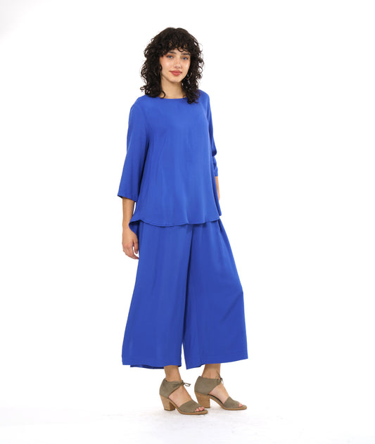 model in a wide leg periwinkle pant with a side slit on either side, worn with a matching pullover top with 3/4 sleeves and a rounded hem, dipping lower in the back