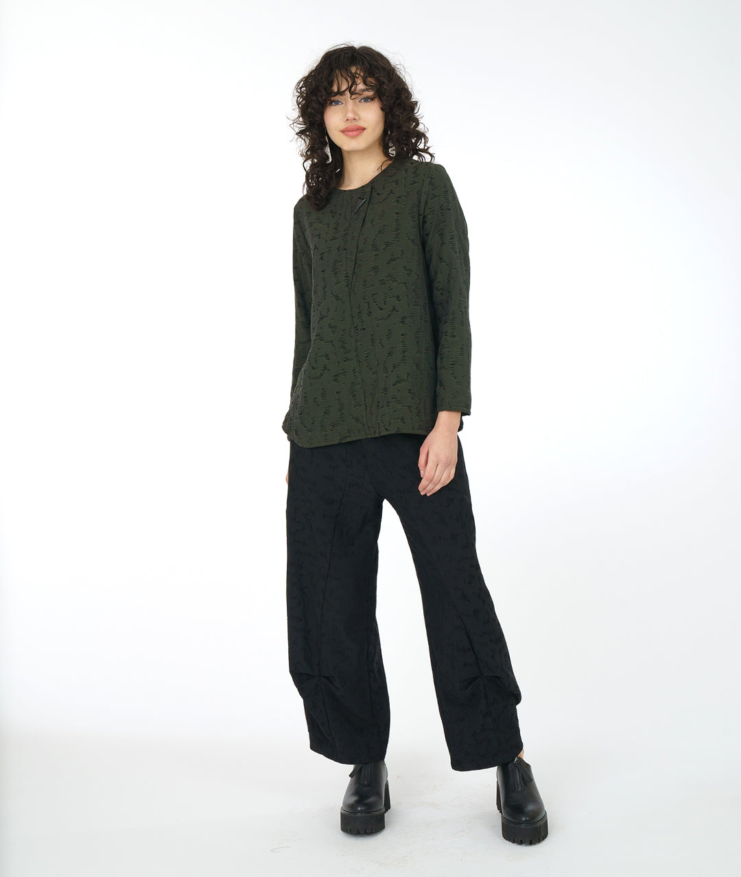 model in a wide leg black pant with a matching green pullover top with a rounded neckline, long sleeves, a boxy body and a triangular shaped false placket at the top, held with a single oversized button