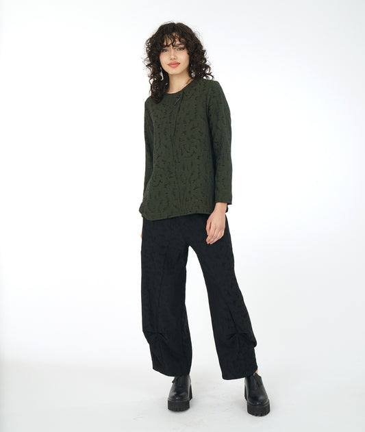 model in a wide leg black pant with a matching green pullover top with a rounded neckline, long sleeves, a boxy body and a triangular shaped false placket at the top, held with a single oversized button