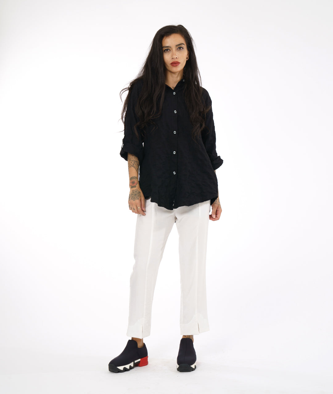 model in a white straight cut pant with a black button down blouse with rolled sleeves
