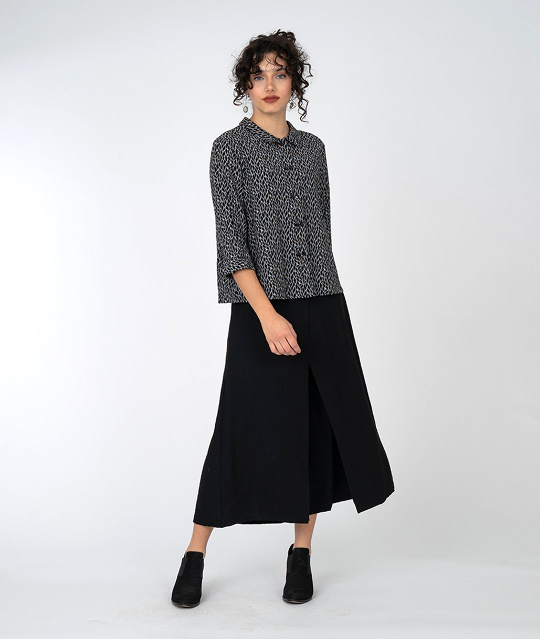 model in a wide leg black pant with an overlapping front, worn with a black and grey leaf print button down with a twin button and 3/4 sleeves