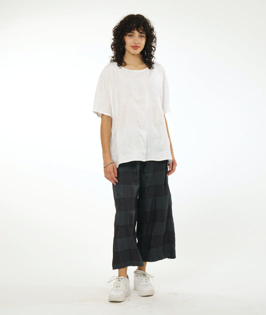 model in a wide leg deep grey pant, white pullover top with a large rounded neckline and an elbow length raglan sleeve. Top and pant both have a large checkered print woven into the fabric