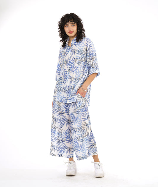 model in a wide leg white pant with a blue and black leaf print. worn with a button down blouse with rolled sleeves in the same fabric
