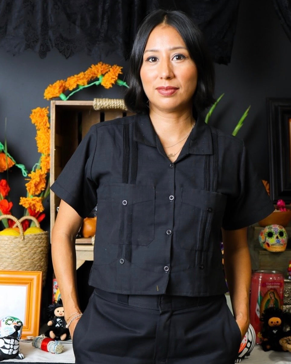 Person wearing a black outfit standing in front of a decorated wall 