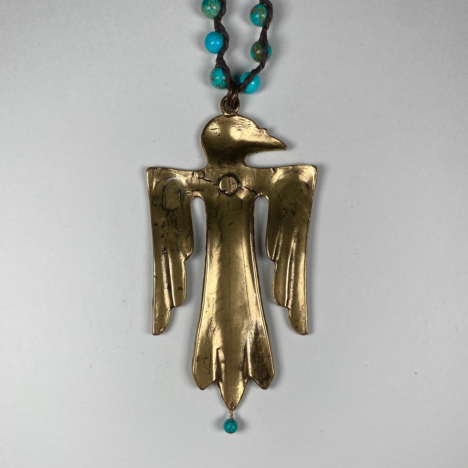 Backside closeup of a Bronze Thunderbird pendant featuring dangling Turquoise bead 