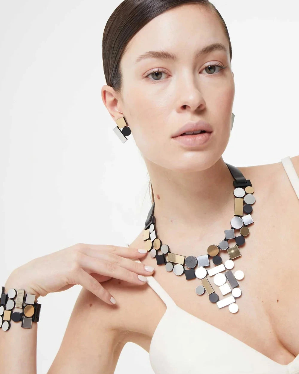 model wearing silver, gold and black geometric shaped necklace, earrings and bracelet against white background