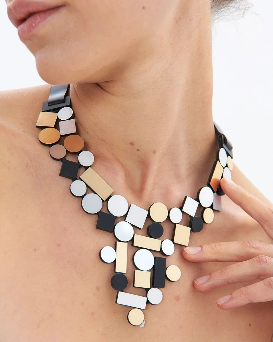 model wearing silver, gold and black geometric shaped necklace against white background