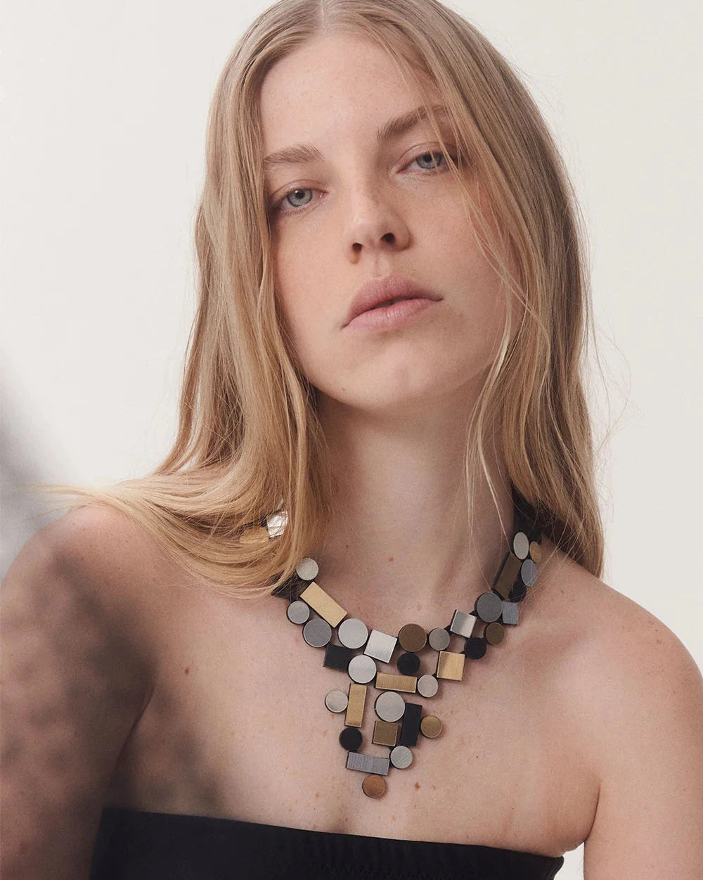 model wearing silver, gold and black geometric shaped necklace against white background