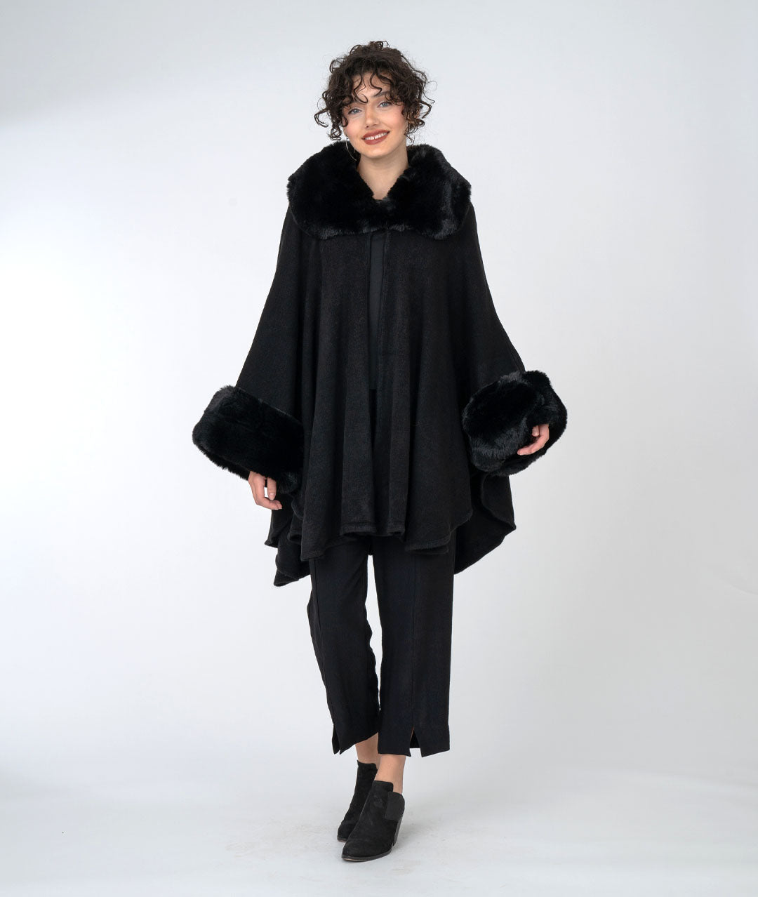 model in an all black outfit with a rich black cape with faux fur sleeves and collar, buttoned at the neck