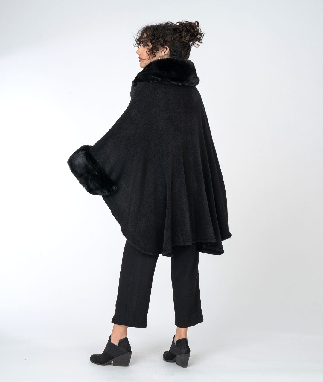 model in an all black outfit with a rich black cape with faux fur sleeves and collar, buttoned at the neck
