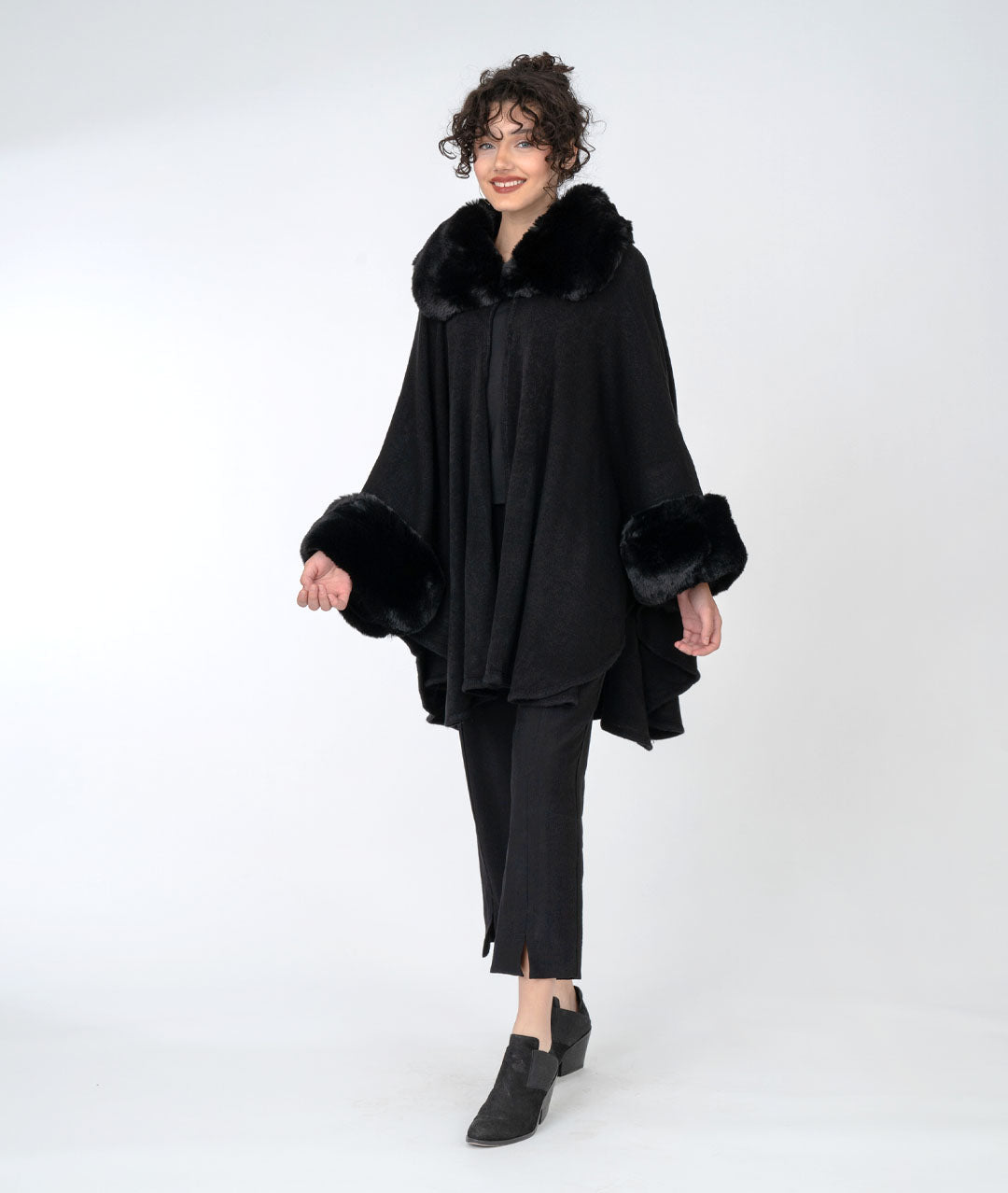 model in an all black outfit with a rich black cape with faux fur sleeves and collar, buttoned at the neck